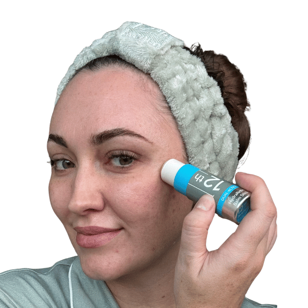 Woman applying skincare product with a towel on her head against a white background